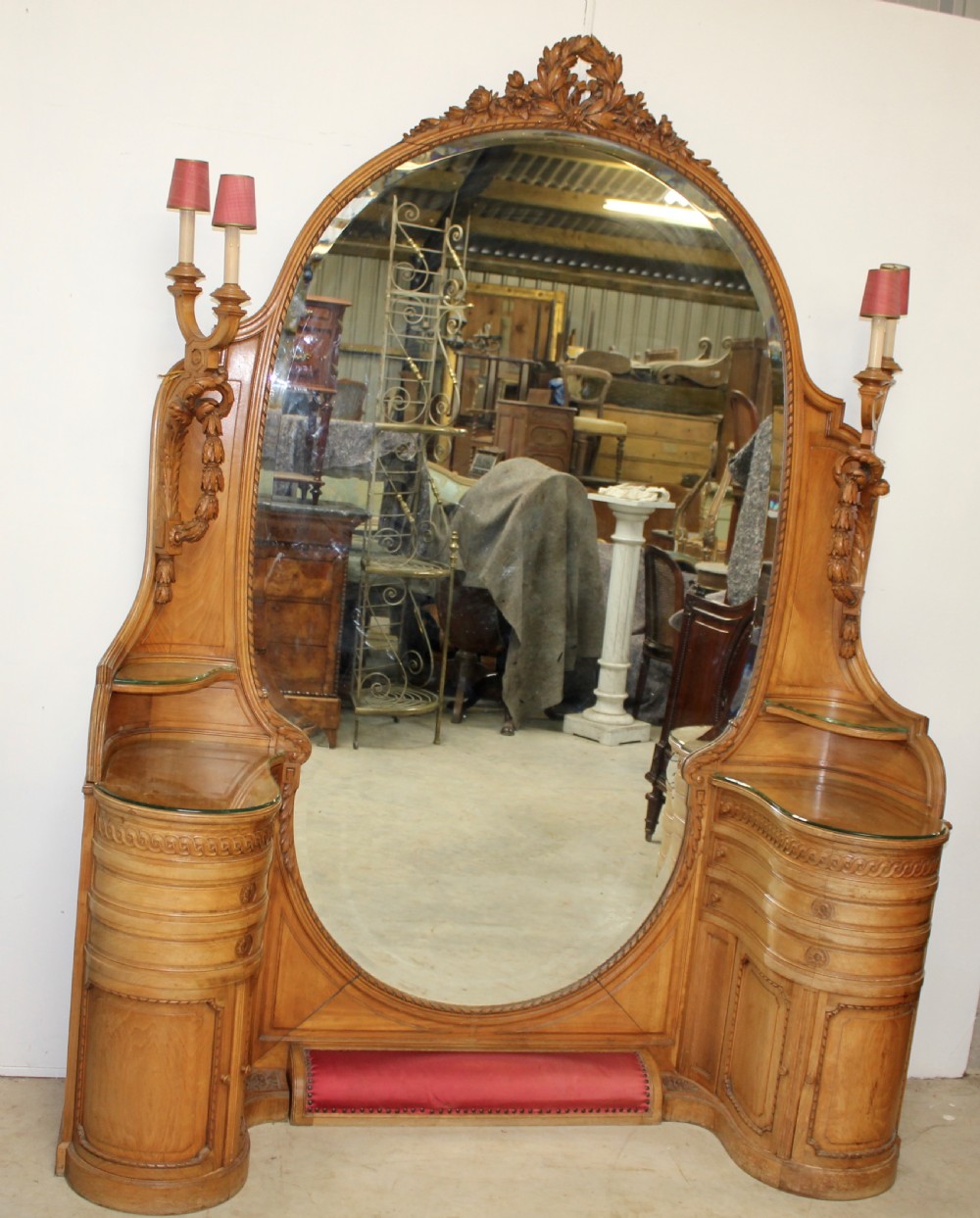A French carved walnut dressing table featuring a large central oval mirror, twin side sconces with fabric shades, pedestals with glass tops, and a low red velvet footrest. View II