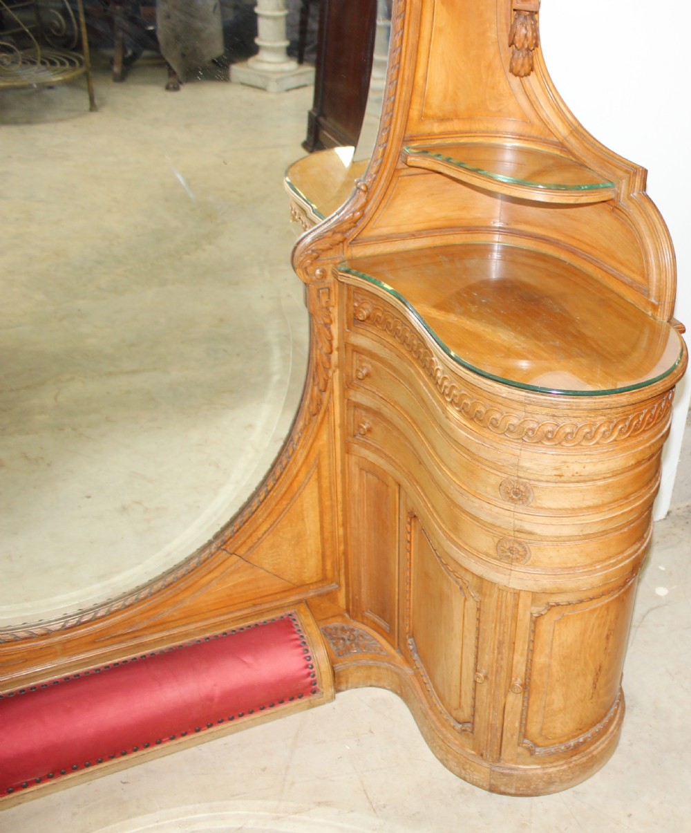 A French carved walnut dressing table featuring a large central oval mirror, twin side sconces with fabric shades, pedestals with glass tops, and a low red velvet footrest. View VI