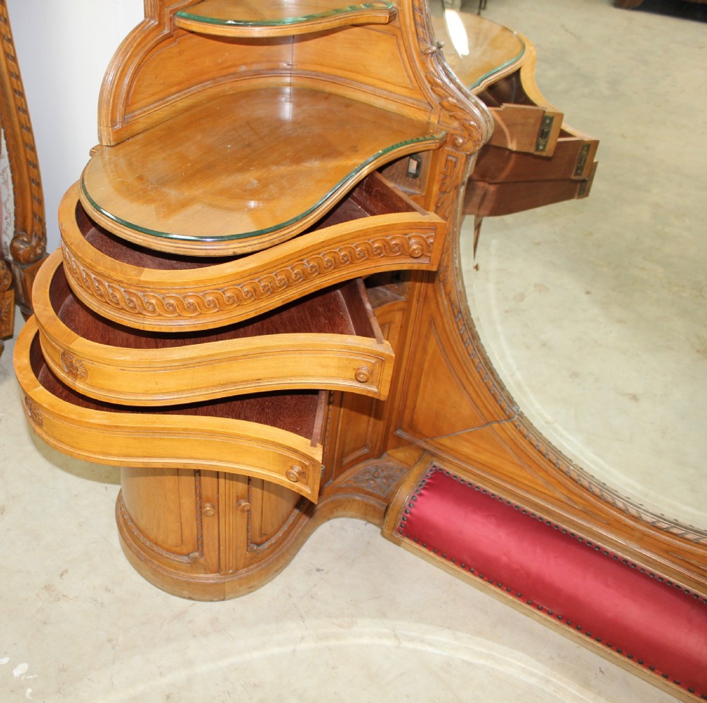 A French carved walnut dressing table featuring a large central oval mirror, twin side sconces with fabric shades, pedestals with glass tops, and a low red velvet footrest. View VII