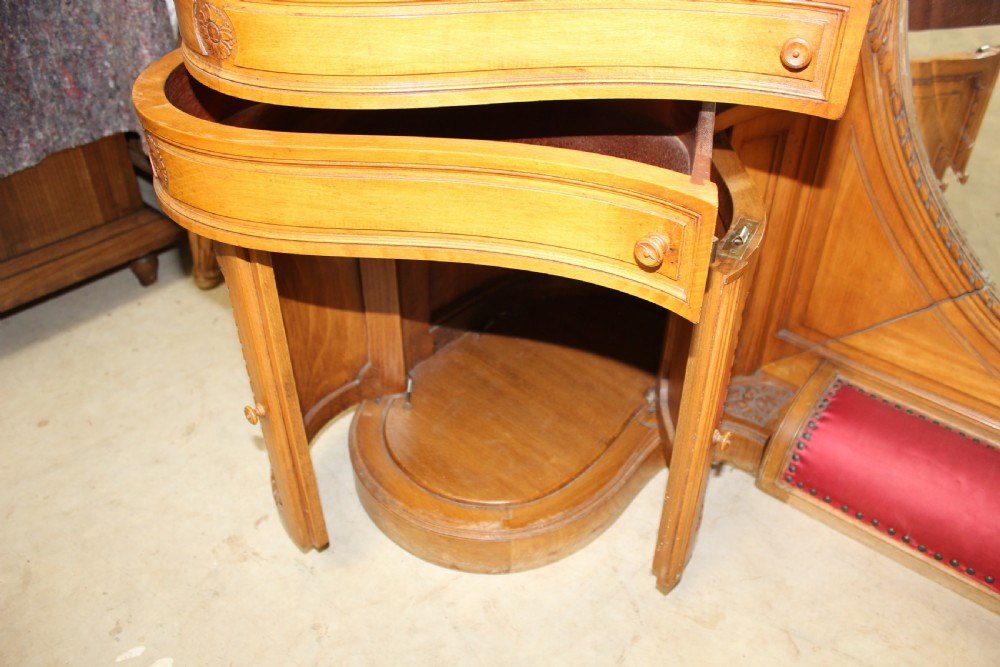 A French carved walnut dressing table featuring a large central oval mirror, twin side sconces with fabric shades, pedestals with glass tops, and a low red velvet footrest. View IX