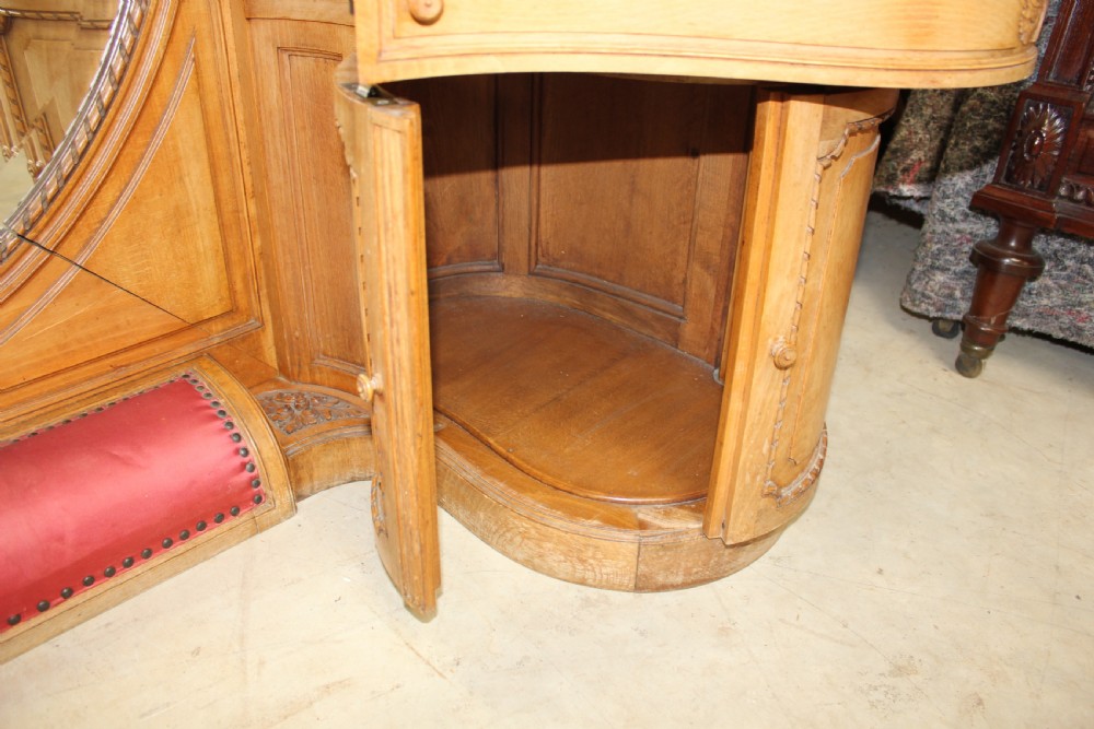 A French carved walnut dressing table featuring a large central oval mirror, twin side sconces with fabric shades, pedestals with glass tops, and a low red velvet footrest. View X