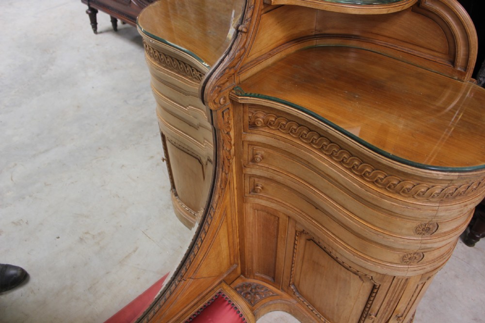 A French carved walnut dressing table featuring a large central oval mirror, twin side sconces with fabric shades, pedestals with glass tops, and a low red velvet footrest. View XV