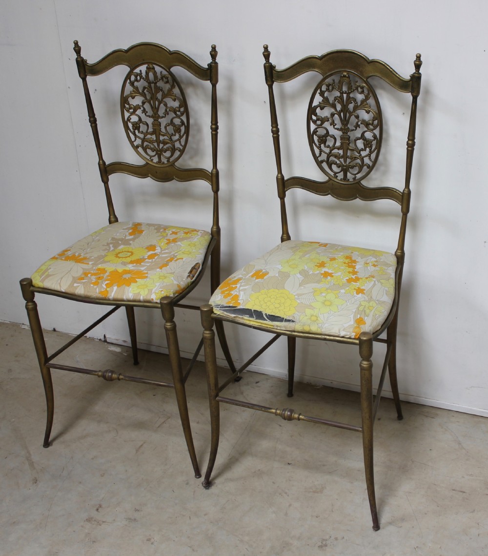 A pair of gold-toned brass side chairs featuring oval openwork splat backs, turned stretchers, and yellow floral fabric seats. View II