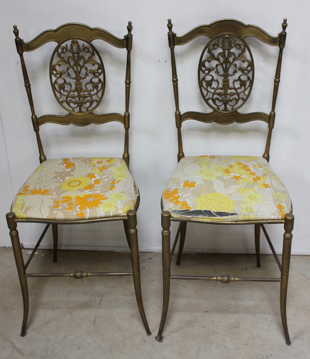 A pair of gold-toned brass side chairs featuring oval openwork splat backs, turned stretchers, and yellow floral fabric seats. View V