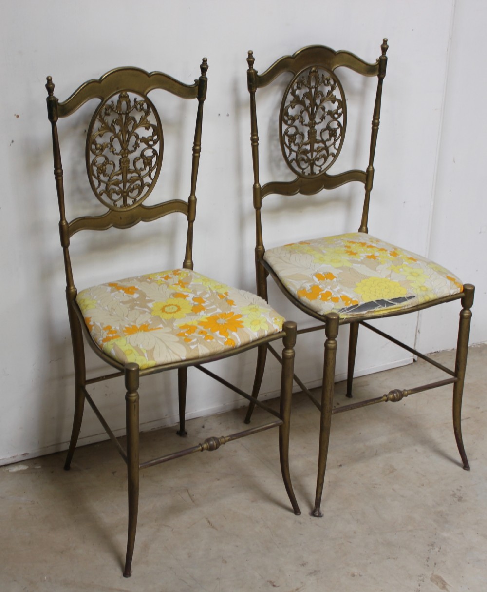 A pair of gold-toned brass side chairs featuring oval openwork splat backs, turned stretchers, and yellow floral fabric seats. View VI