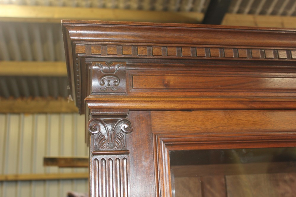 A large antique warm brown wooden breakfront bookcase with three glazed doors, carved fluted pilasters, and lower drawers. View IV