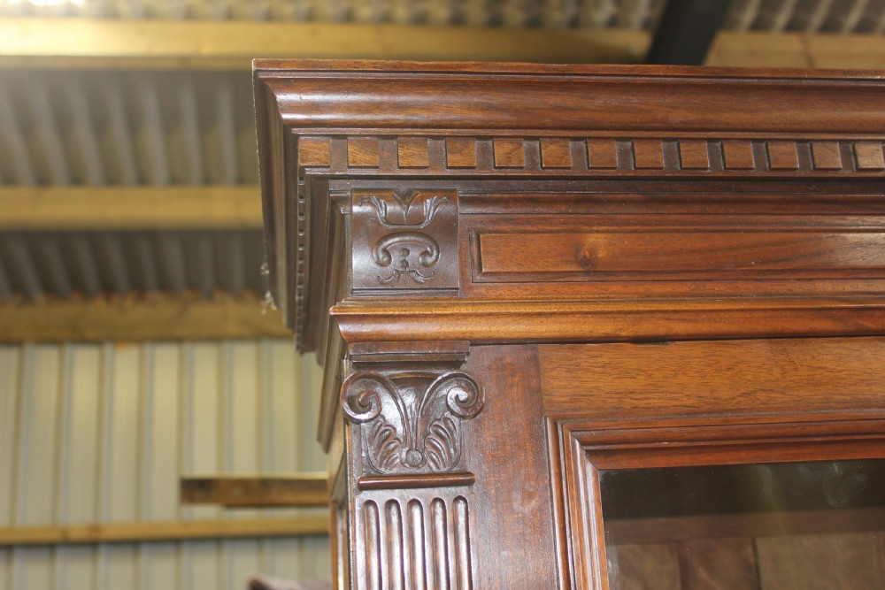 A large antique warm brown wooden breakfront bookcase with three glazed doors, carved fluted pilasters, and lower drawers. View V