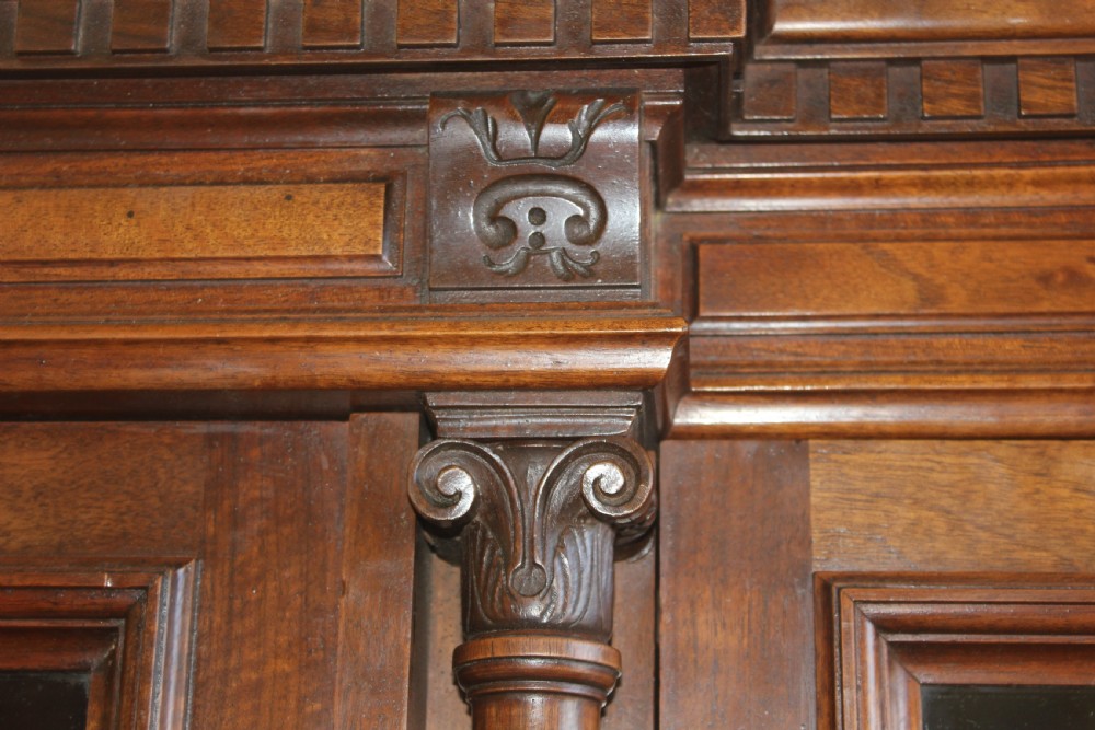 A large antique warm brown wooden breakfront bookcase with three glazed doors, carved fluted pilasters, and lower drawers. View VI