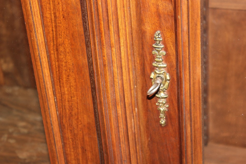 A large antique warm brown wooden breakfront bookcase with three glazed doors, carved fluted pilasters, and lower drawers. View VII
