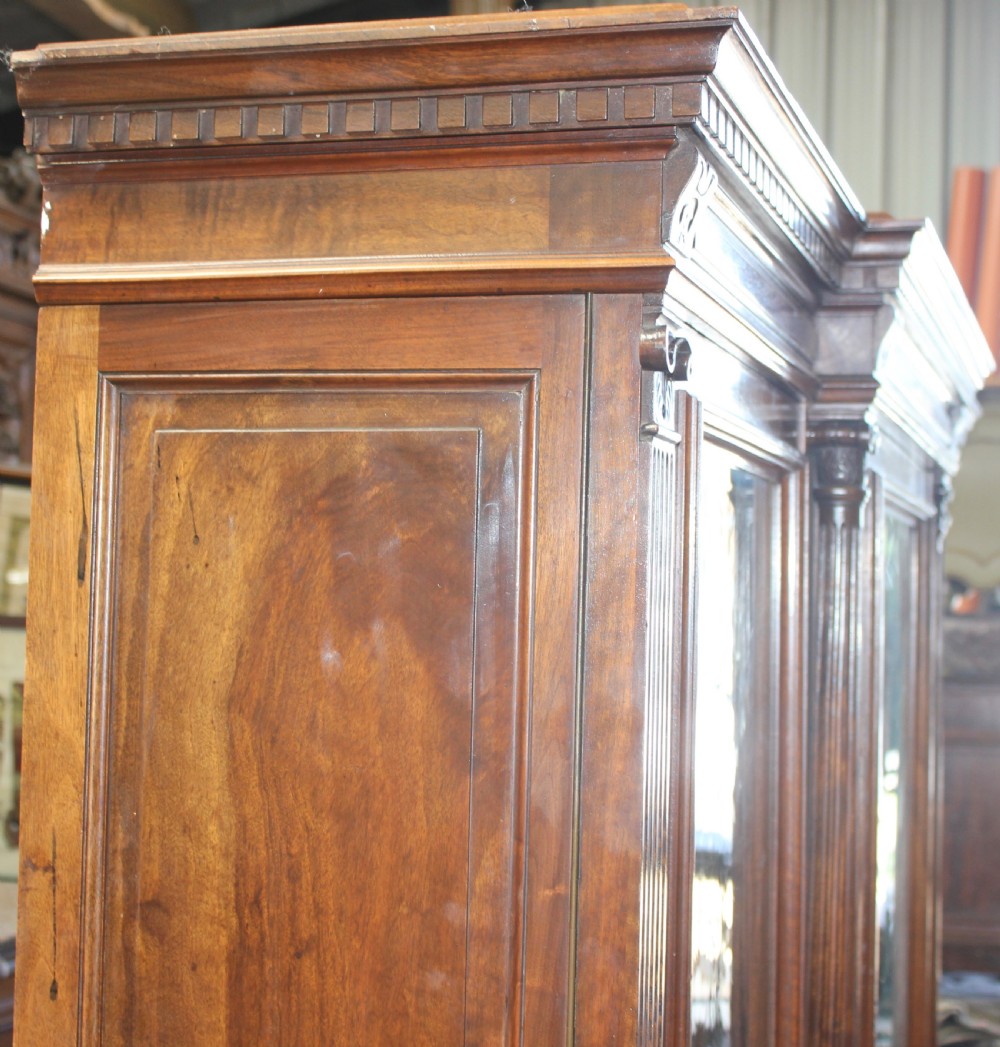 A large antique warm brown wooden breakfront bookcase with three glazed doors, carved fluted pilasters, and lower drawers. View VIII