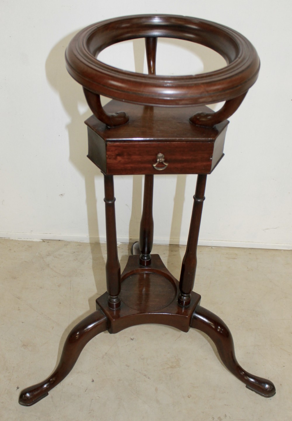 A dark mahogany Georgian tripod washstand featuring a circular top ring, central drawer tier, and curved tripod legs.