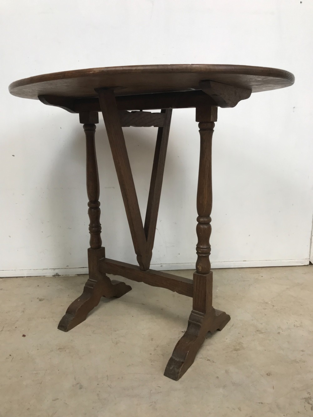 A dark oak miniature wine table featuring an oval top resting on turned vertical posts and a V-shaped support on trestle feet.
