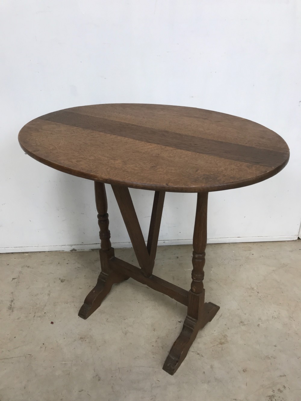 A dark oak miniature wine table featuring an oval top resting on turned vertical posts and a V-shaped support on trestle feet. View III