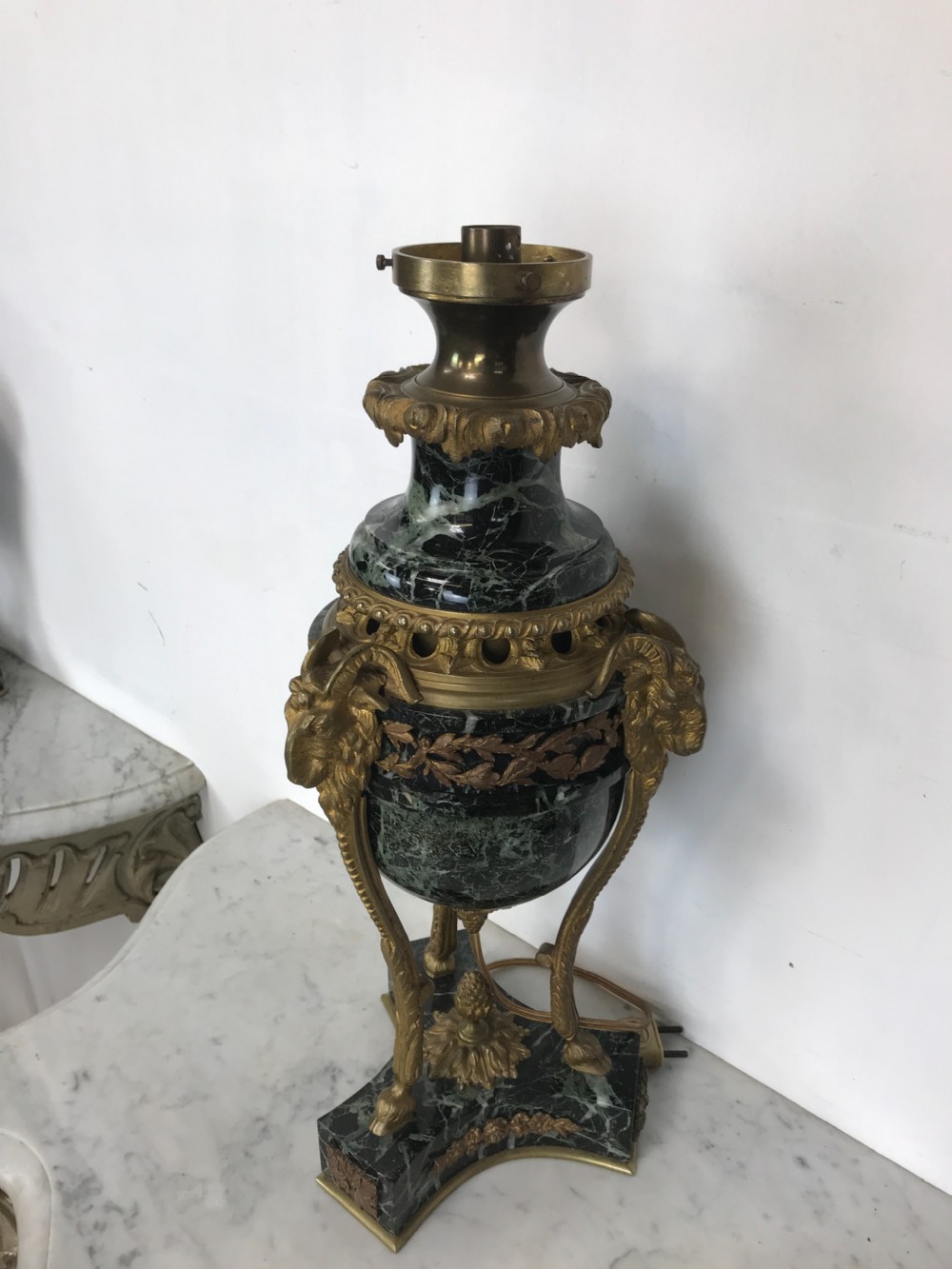 A pair of Neoclassical style table lamps fashioned as dark green marble urns supported by gilt bronze triform legs featuring rams head mounts. View II