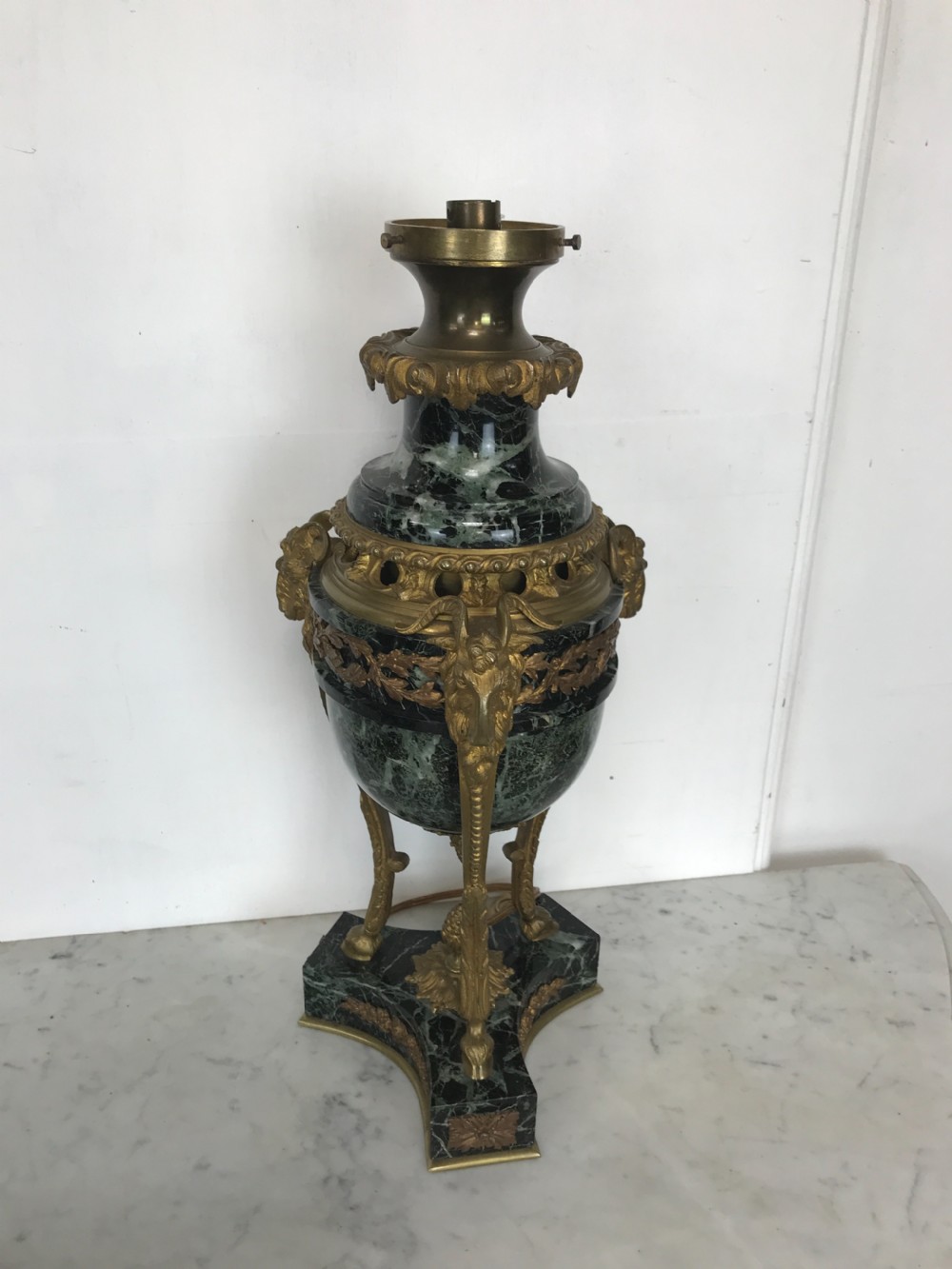 A pair of Neoclassical style table lamps fashioned as dark green marble urns supported by gilt bronze triform legs featuring rams head mounts. View V