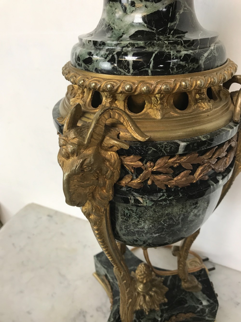 A pair of Neoclassical style table lamps fashioned as dark green marble urns supported by gilt bronze triform legs featuring rams head mounts. View VI