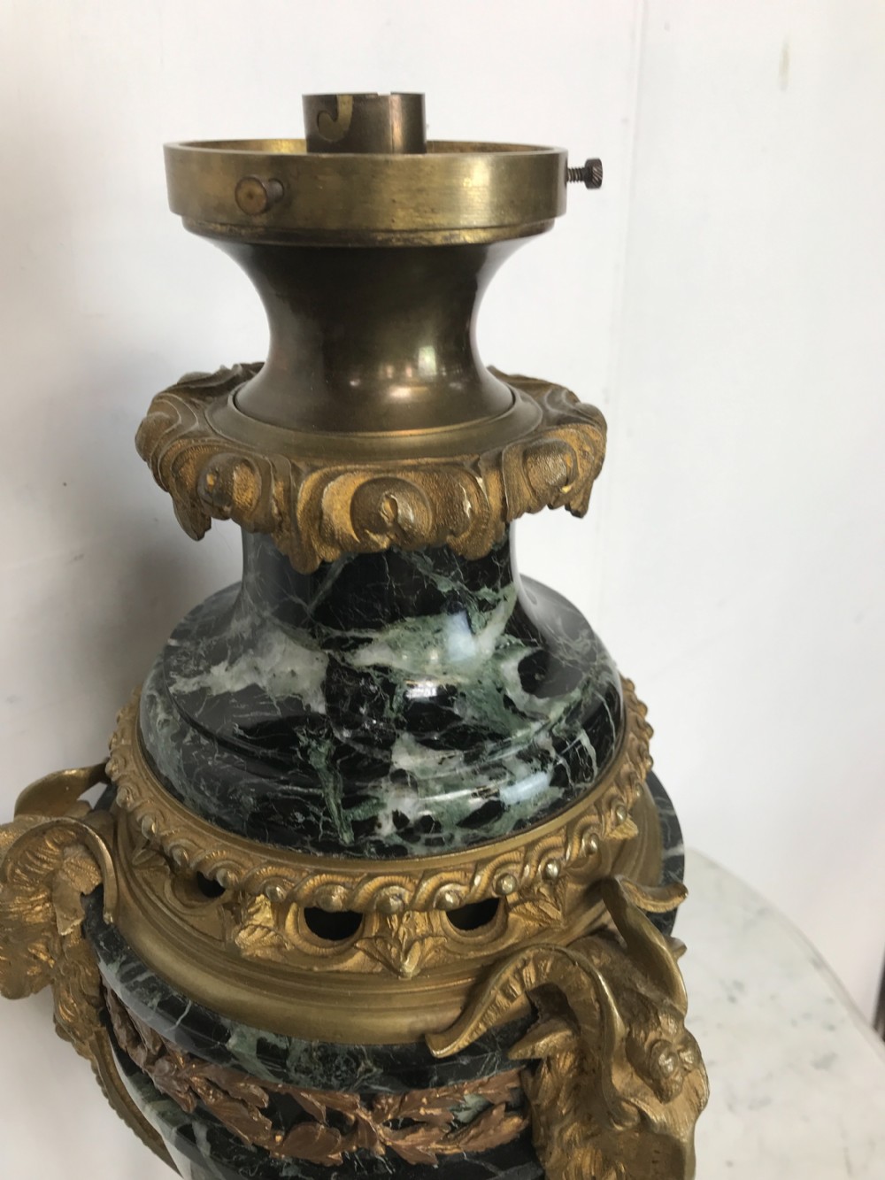 A pair of Neoclassical style table lamps fashioned as dark green marble urns supported by gilt bronze triform legs featuring rams head mounts. View IX