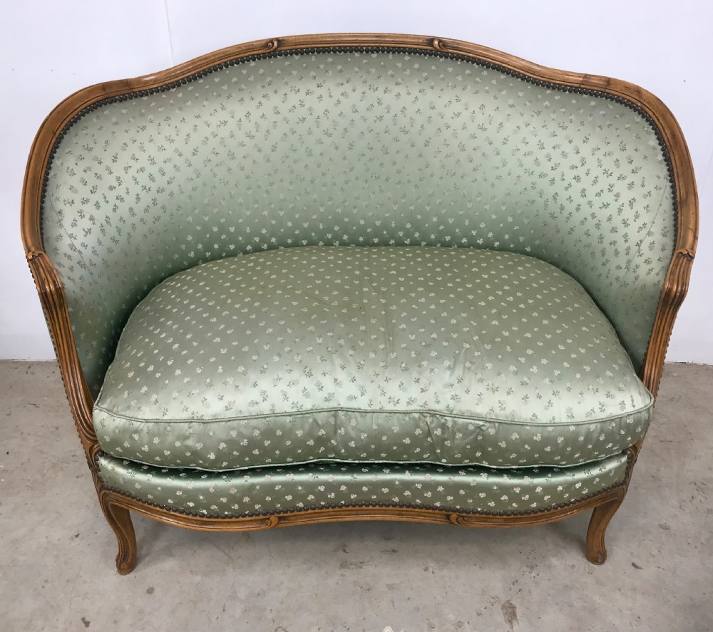 An antique French Louis XV style settee featuring a curved carved wooden frame and sage green patterned fabric upholstery with decorative studding.