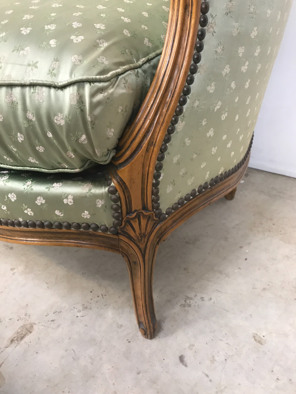 An antique French Louis XV style settee featuring a curved carved wooden frame and sage green patterned fabric upholstery with decorative studding. View II