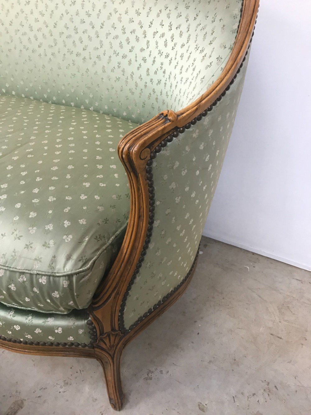 An antique French Louis XV style settee featuring a curved carved wooden frame and sage green patterned fabric upholstery with decorative studding. View III