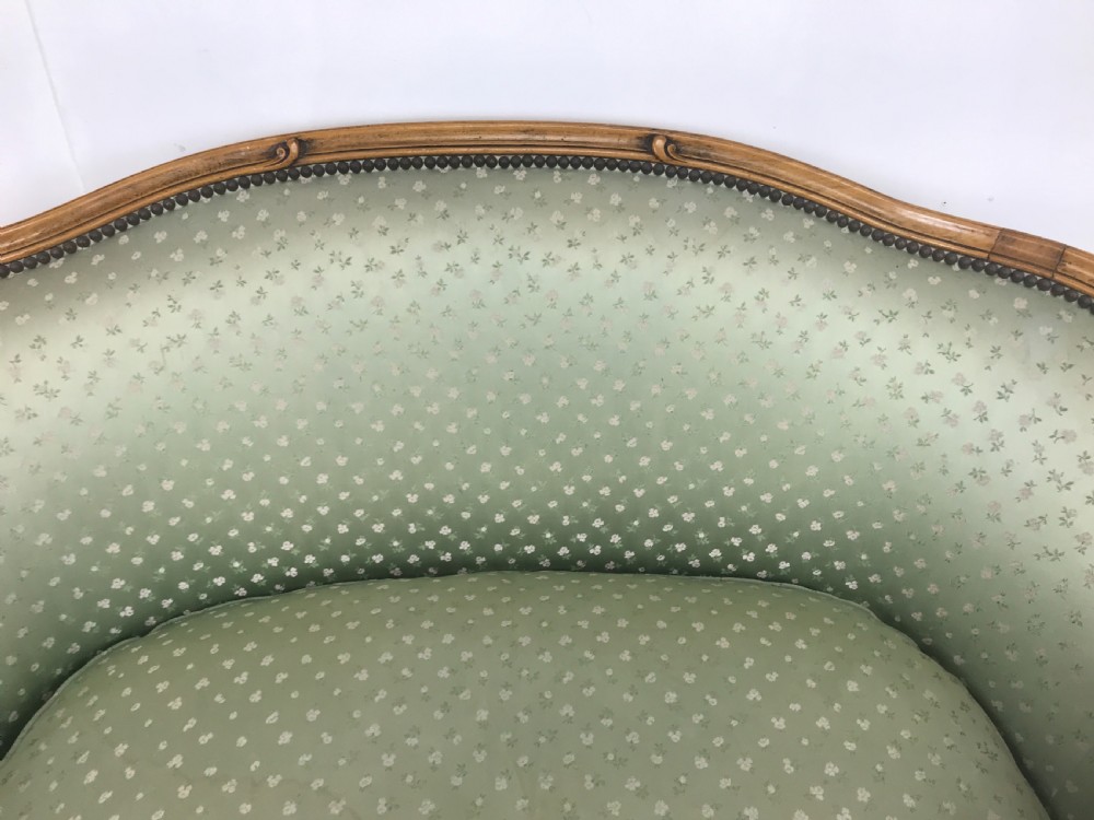 An antique French Louis XV style settee featuring a curved carved wooden frame and sage green patterned fabric upholstery with decorative studding. View V