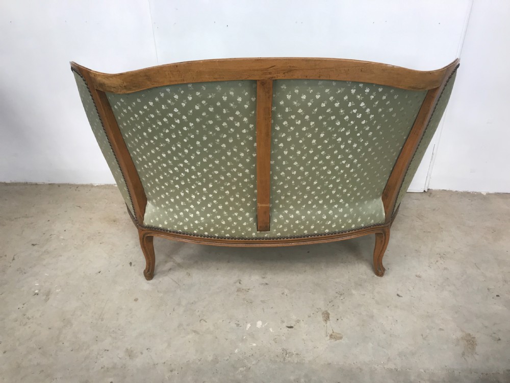 An antique French Louis XV style settee featuring a curved carved wooden frame and sage green patterned fabric upholstery with decorative studding. View VI