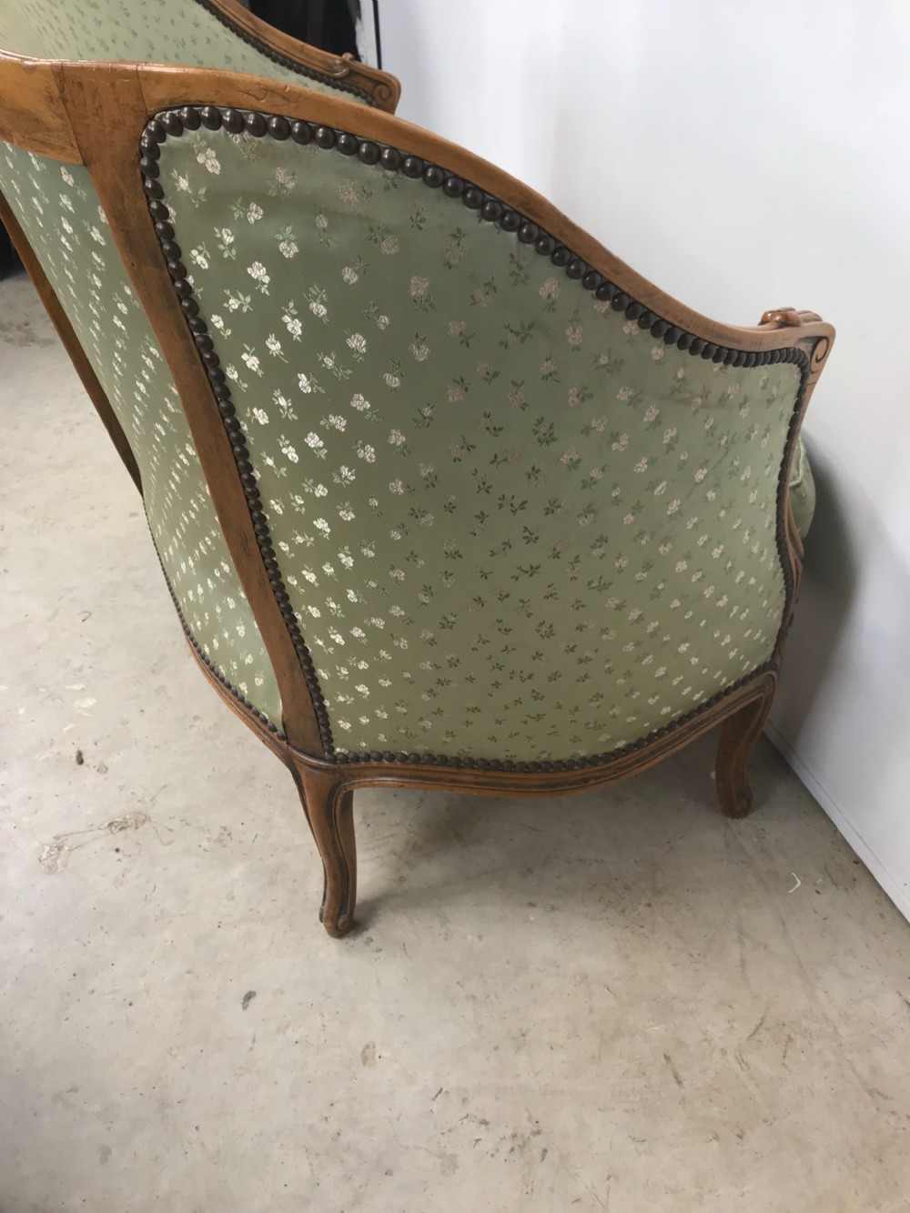 An antique French Louis XV style settee featuring a curved carved wooden frame and sage green patterned fabric upholstery with decorative studding. View VII