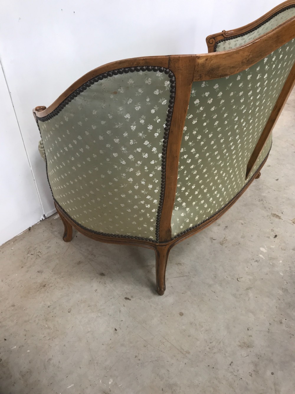 An antique French Louis XV style settee featuring a curved carved wooden frame and sage green patterned fabric upholstery with decorative studding. View VIII