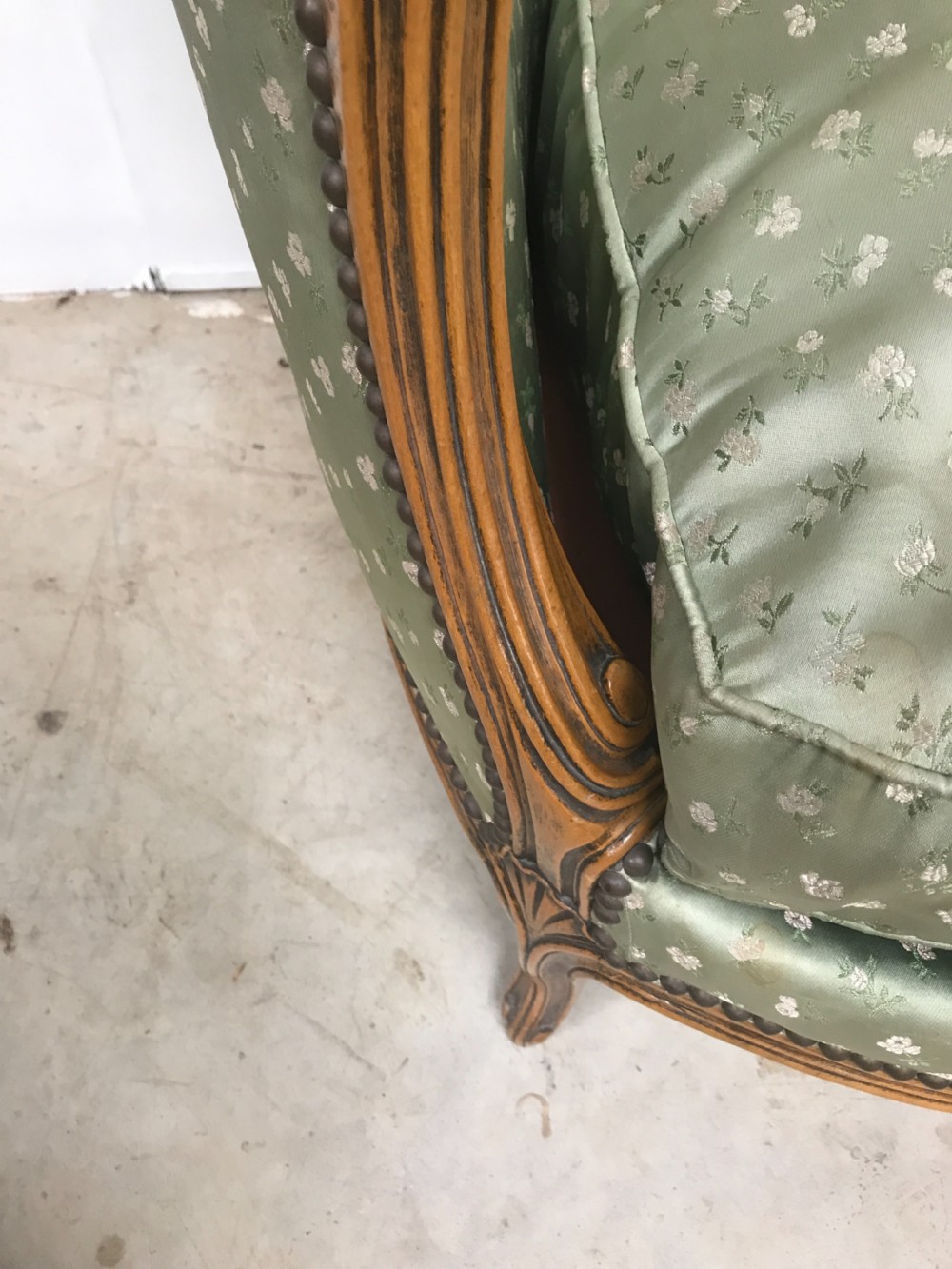 An antique French Louis XV style settee featuring a curved carved wooden frame and sage green patterned fabric upholstery with decorative studding. View IX