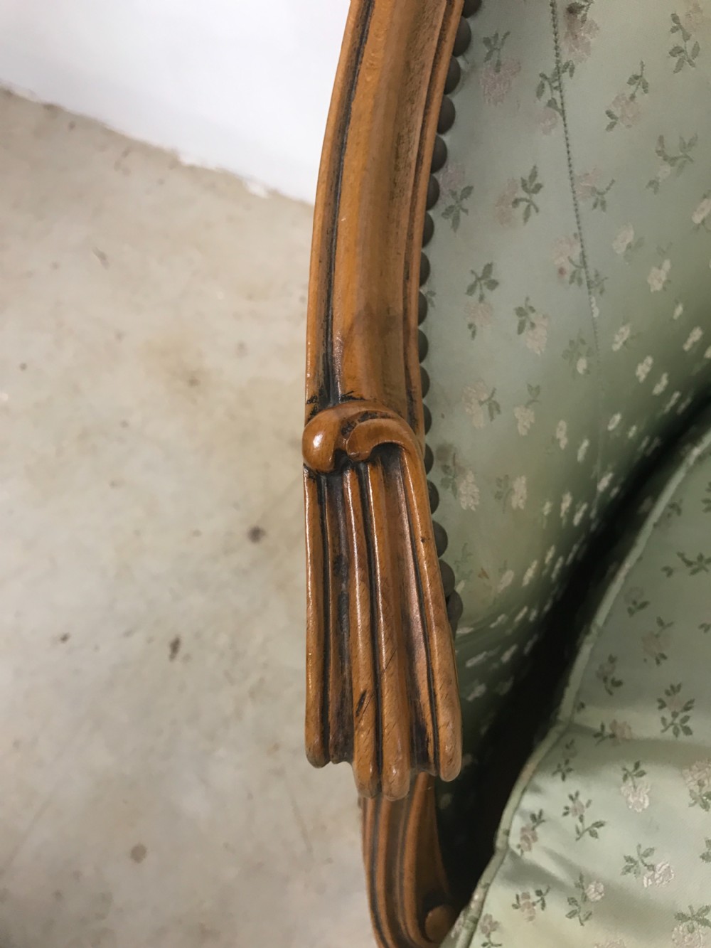 An antique French Louis XV style settee featuring a curved carved wooden frame and sage green patterned fabric upholstery with decorative studding. View X
