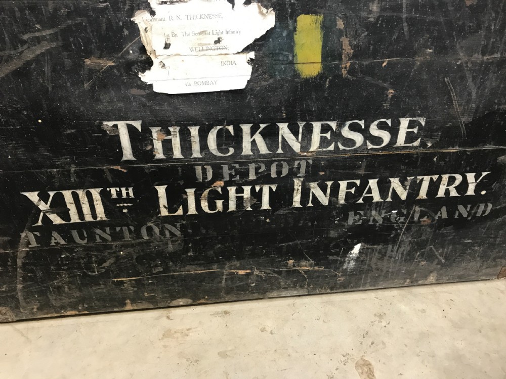 Two stacked dark painted antique wooden military trunks featuring original stencilled regimental lettering and iron brackets. View II