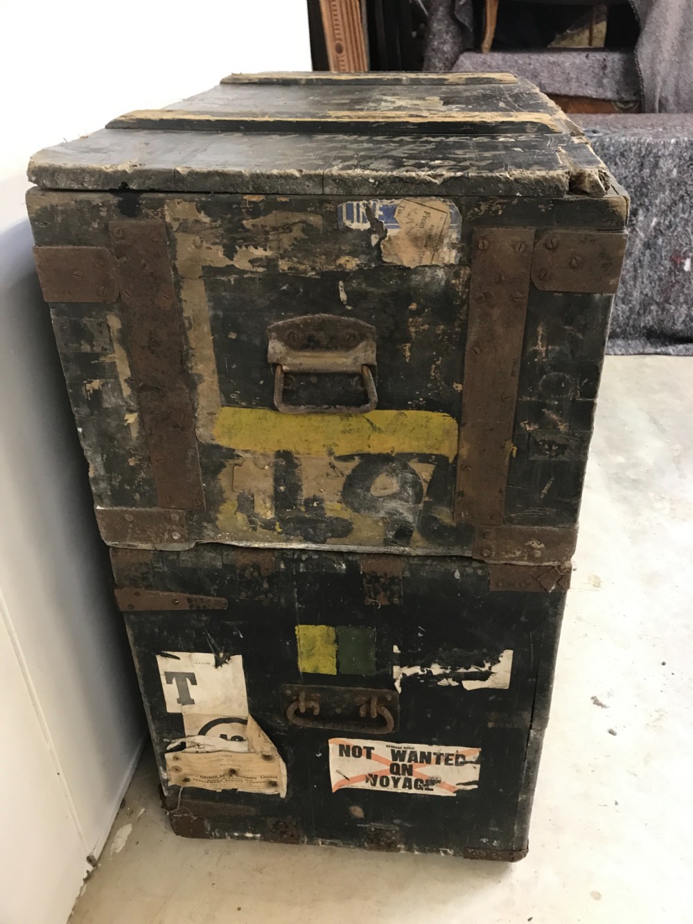 Two stacked dark painted antique wooden military trunks featuring original stencilled regimental lettering and iron brackets. View IV