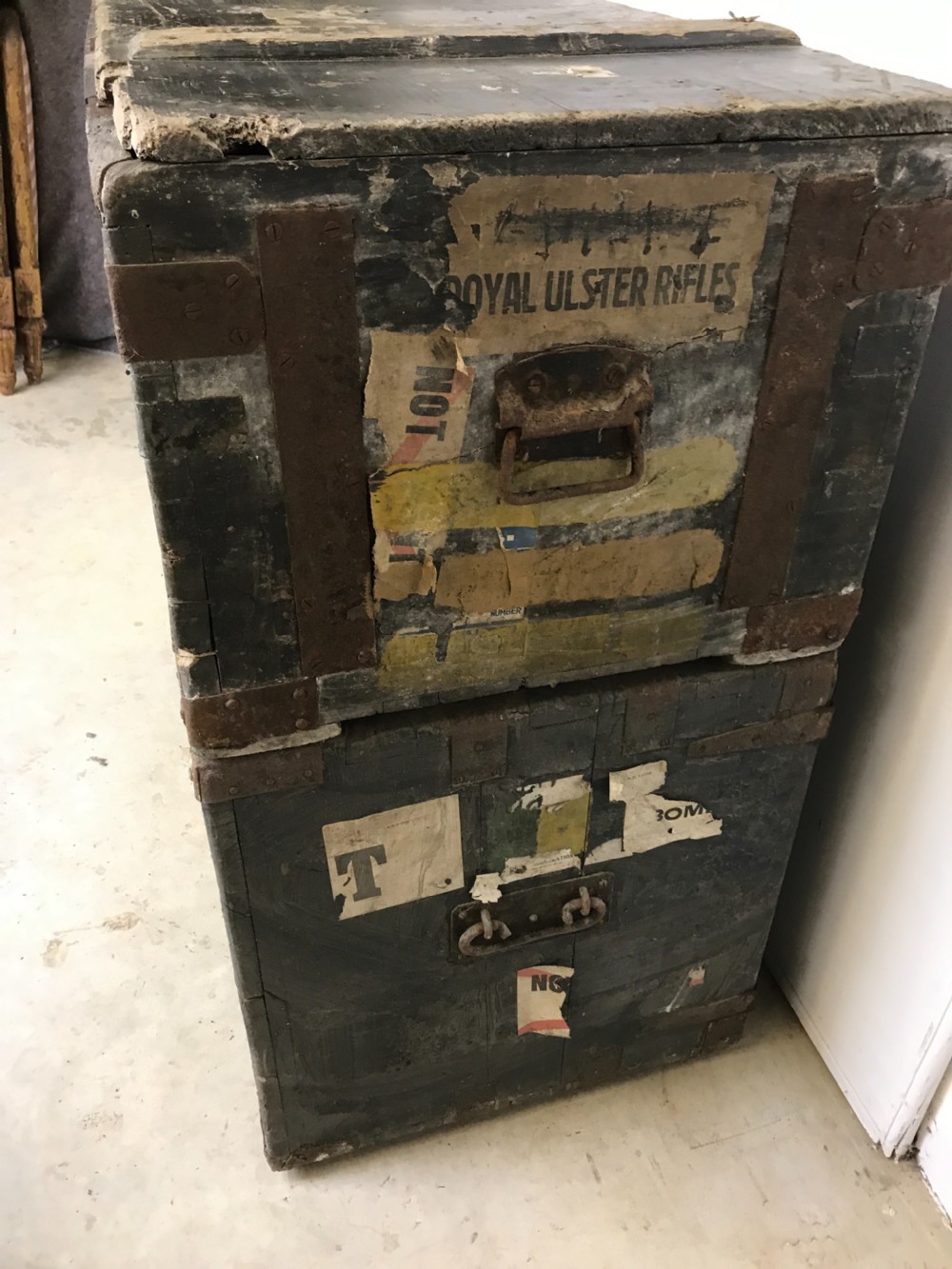 Two stacked dark painted antique wooden military trunks featuring original stencilled regimental lettering and iron brackets. View V