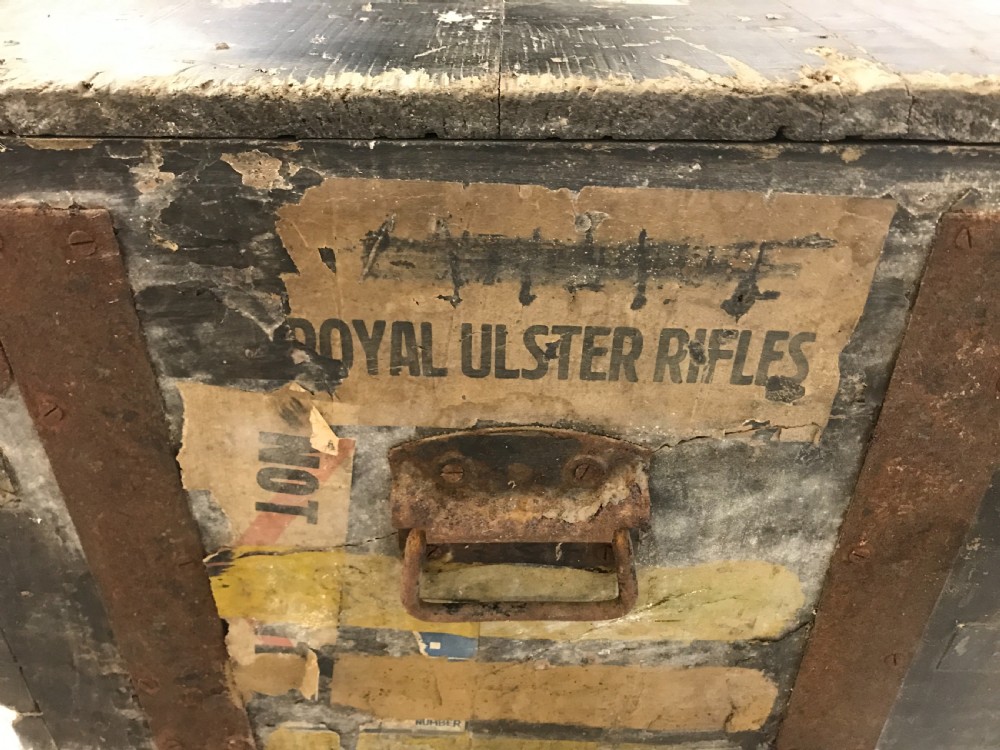 Two stacked dark painted antique wooden military trunks featuring original stencilled regimental lettering and iron brackets. View VI