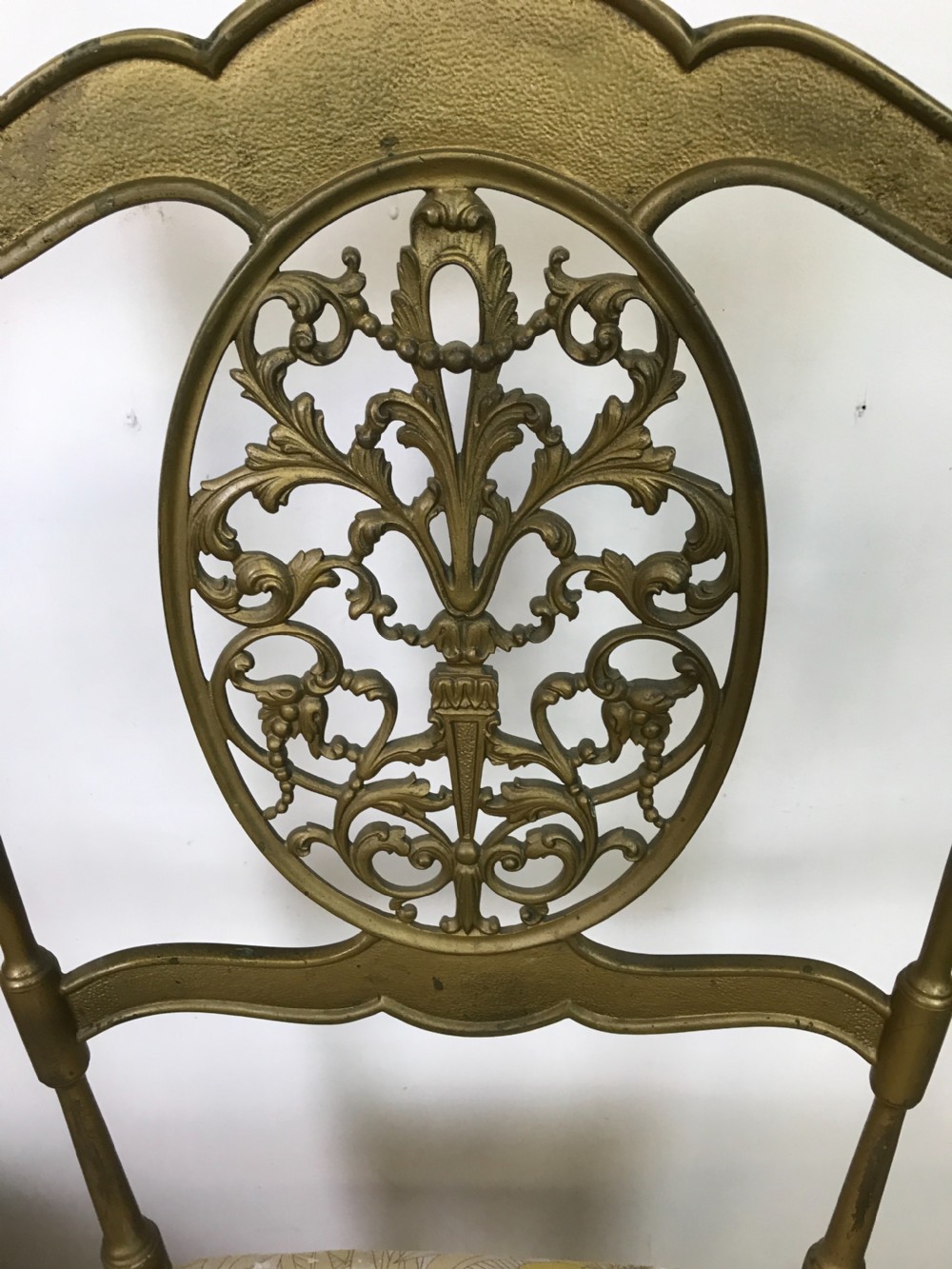 A pair of solid brass side chairs featuring ornate openwork oval backrests, slender turned legs, and yellow floral upholstered seats. View III