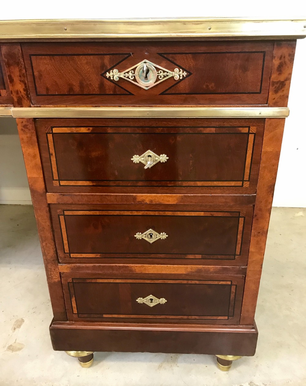 An antique mahogany pedestal desk featuring a dark leather writing top, multiple drawers with brass keyhole escutcheons, and central metal mounts. View II