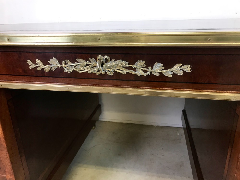 An antique mahogany pedestal desk featuring a dark leather writing top, multiple drawers with brass keyhole escutcheons, and central metal mounts. View IV