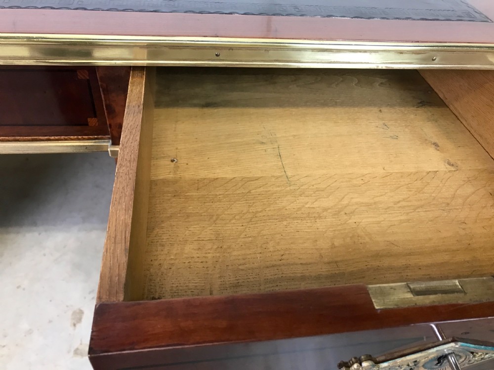 An antique mahogany pedestal desk featuring a dark leather writing top, multiple drawers with brass keyhole escutcheons, and central metal mounts. View V