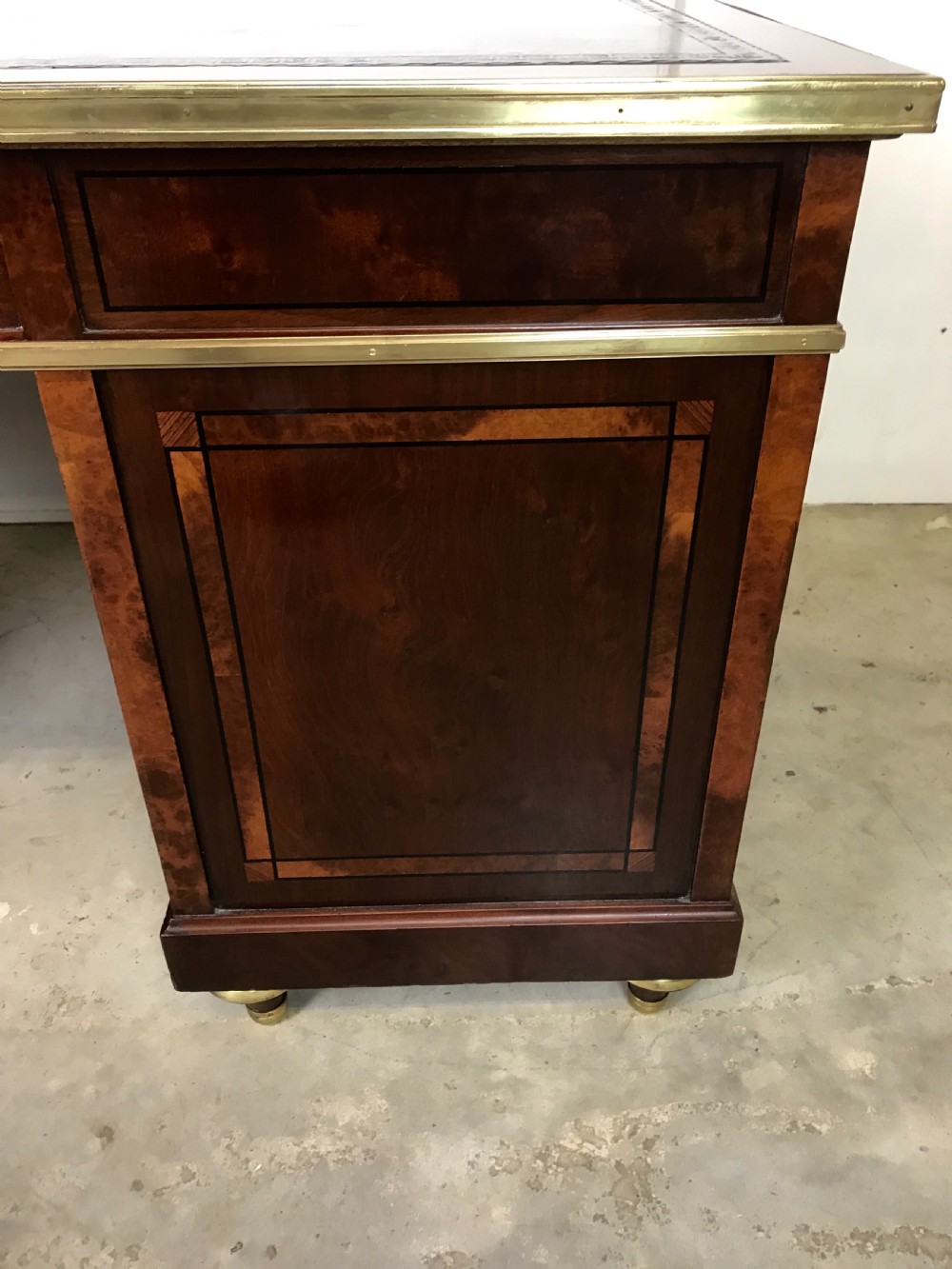 An antique mahogany pedestal desk featuring a dark leather writing top, multiple drawers with brass keyhole escutcheons, and central metal mounts. View XI