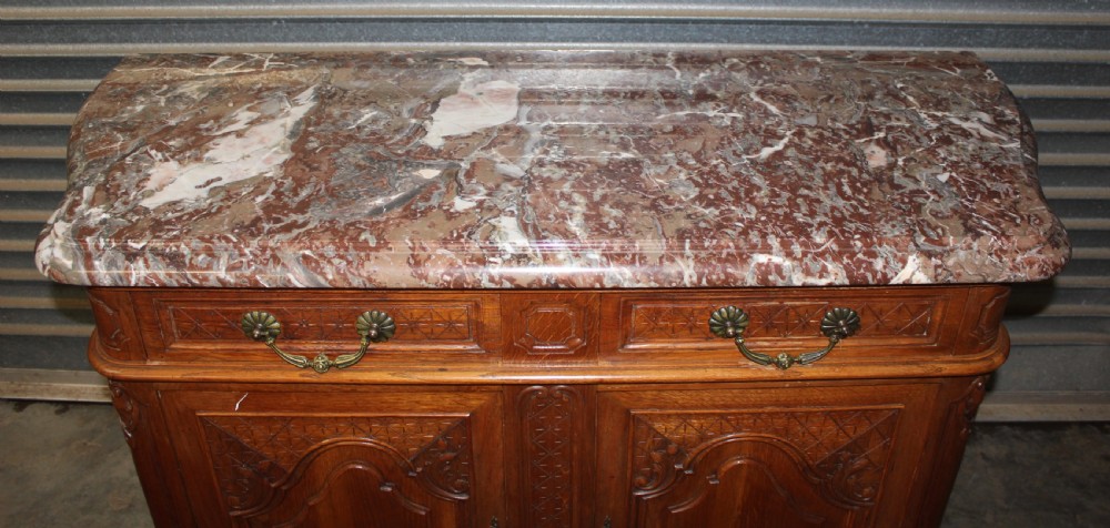 A carved French provincial oak sideboard featuring two drawers, two cabinet doors, carved geometric and floral motifs, cabriole feet, and a thick grey veined marble top. View II