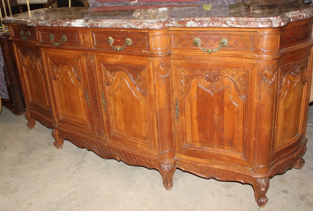 A carved French provincial oak sideboard featuring two drawers, two cabinet doors, carved geometric and floral motifs, cabriole feet, and a thick grey veined marble top. View VII