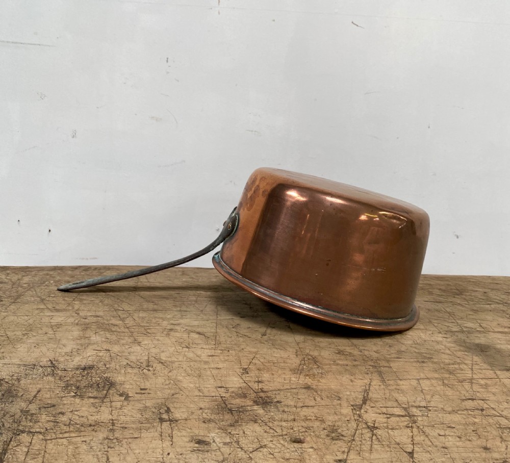 A 19th-century copper saucepan with a polished copper body, rolled rim, and a curved dark iron handle riveted to the side.
