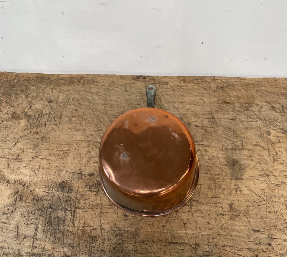 A 19th-century copper saucepan with a polished copper body, rolled rim, and a curved dark iron handle riveted to the side. View IV