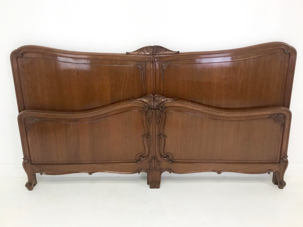 A carved mahogany king size bed frame featuring an arched headboard and matching footboard with intricate foliate detailing and cabriole feet.