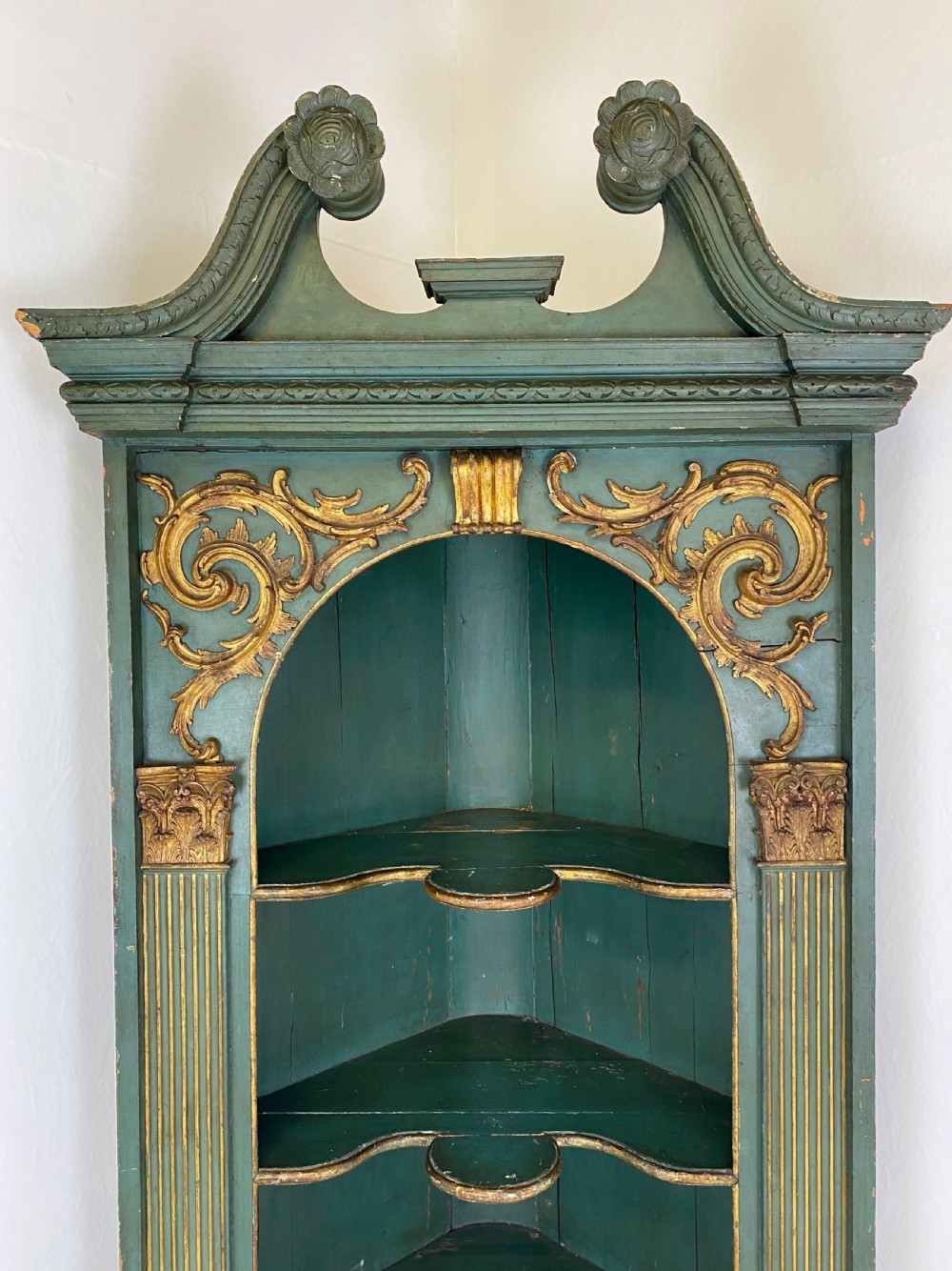 An 18th-century floor-standing teal green open corner cupboard featuring gold leaf detailing, fluted pilasters, and a broken swan-neck pediment. View III