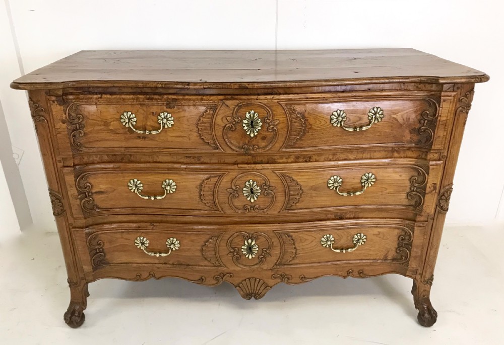An 18th-century French provincial burr ash commode featuring three drawers with carved rocaille motifs, original brass handles, and cabriole legs.