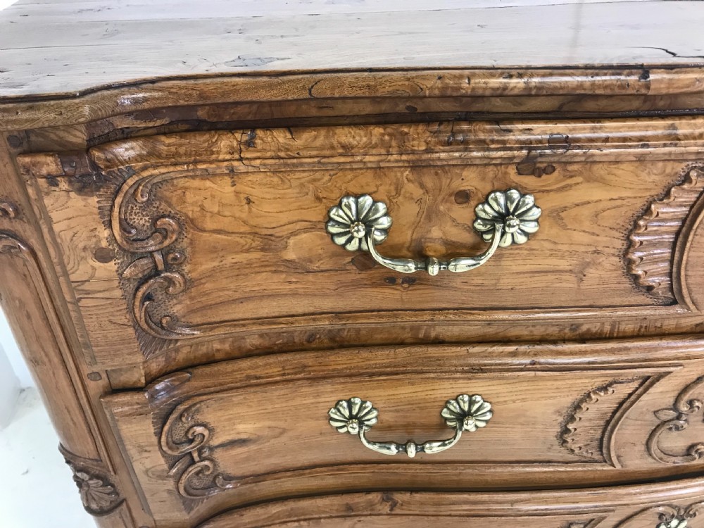 An 18th-century French provincial burr ash commode featuring three drawers with carved rocaille motifs, original brass handles, and cabriole legs. View II
