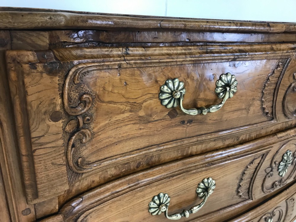 An 18th-century French provincial burr ash commode featuring three drawers with carved rocaille motifs, original brass handles, and cabriole legs. View IV