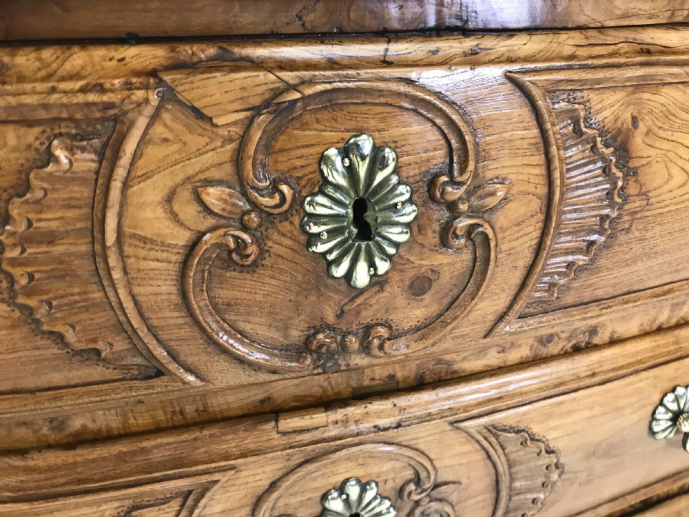 An 18th-century French provincial burr ash commode featuring three drawers with carved rocaille motifs, original brass handles, and cabriole legs. View V