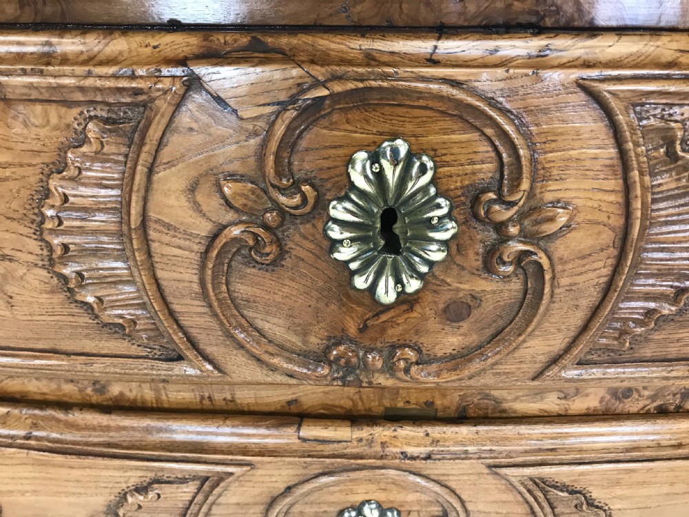 An 18th-century French provincial burr ash commode featuring three drawers with carved rocaille motifs, original brass handles, and cabriole legs. View X